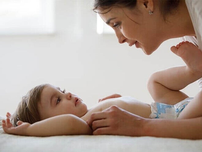 Photo: woman leaning over infant on back, making eye contact in bright room
