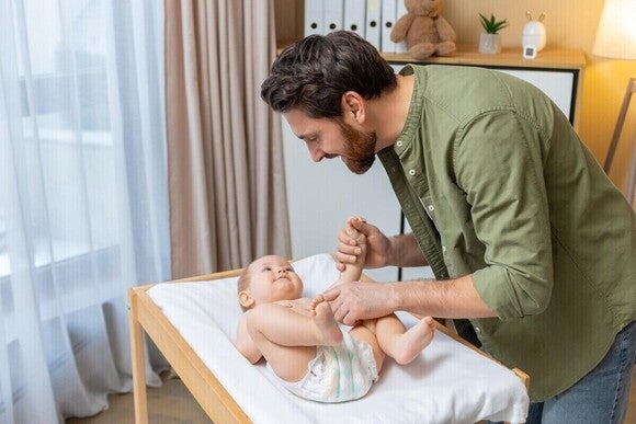 Photograph: father changing diaper, holding smiling baby on nursery changing table